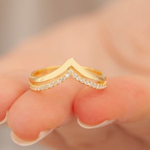 May include: A gold ring with a V-shaped design and a row of small clear stones around the band.