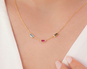Puede incluir: Un collar de cadena dorada con tres piedras preciosas rectangulares: azul, rojo y negro.
