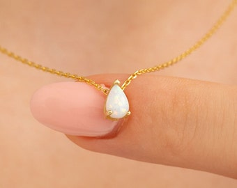May include: A delicate gold chain necklace with a teardrop-shaped opal pendant.