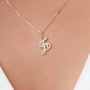 Puede incluir: Un collar de cadena de oro con un colgante de letra cursiva engastado con diamantes.