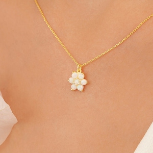 Puede incluir: Un collar de cadena de oro con un delicado colgante de flor con piedras de ópalo blanco.