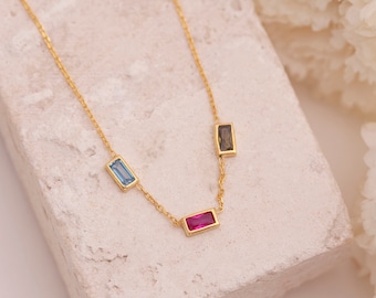 Puede incluir: Un collar de cadena de oro con tres piedras preciosas rectangulares. Las piedras preciosas son azules, marrones y rosas.