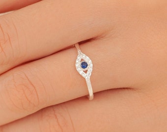May include: Silver ring with a blue evil eye design. The eye is surrounded by small clear stones.