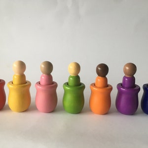 May include: A set of eight wooden nesting dolls, each painted a different colour: red, yellow, pink, green, orange, purple, blue, and brown. The dolls are arranged in a row from left to right, with the largest doll on the left and the smallest doll on the right.