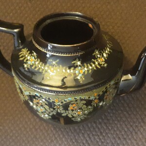 May include: A black teapot with gold and colorful floral designs. The teapot has a round body and a spout on the side.