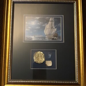 Peut inclure: Une estampe encadrée d'un navire naviguant sur l'océan la nuit. L'estampe est accompagnée d'une pièce d'or et d'un morceau de poterie cassée.