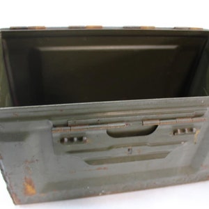 May include: A green metal ammo box with a hinged lid and a rusted exterior. The box is empty and open.
