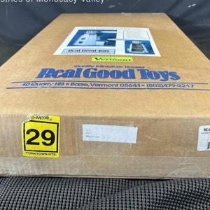 May include: A brown cardboard box with a yellow sticker that says "29 YORKTOWN HTS." The box has a label that says "Real Good Toys" and includes the company's address and phone number. The box is for a miniature house kit.