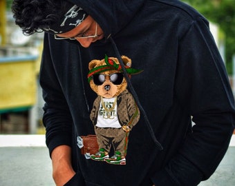 May include: Black hoodie with a graphic print of a cartoon bear wearing sunglasses, a bandana, and a gold chain. The bear is holding a briefcase and wearing a green and brown patterned outfit. The text "Just Get It" is printed on the bear's shirt.