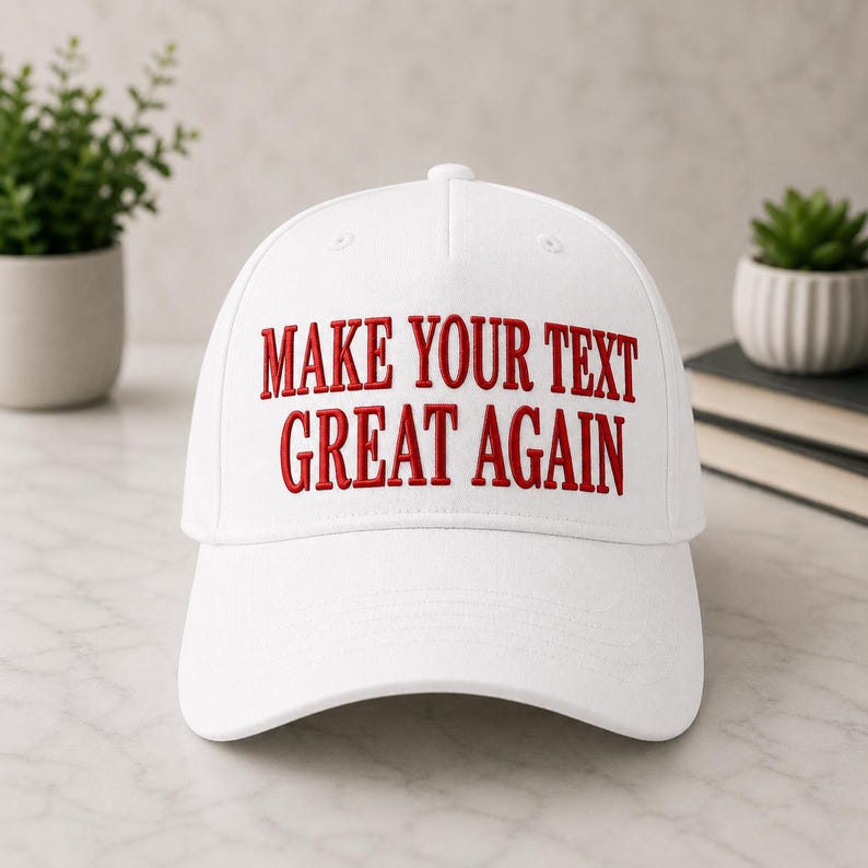 Może przedstawiać: Biała czapka bejsbolowa z wyhaftowanym czerwonym napisem "MAKE YOUR TEXT GREAT AGAIN". Czapka ma zakrzywiony daszek i guzik na g&oacute;rze. Kapelusz jest prezentowany na jasnej powierzchni.