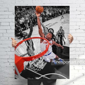 May include: A vertical sports poster featuring a black and white photograph of a basketball game with a vibrant orange hoop and basketball in the foreground. A player in a white New York jersey is shown mid-air attempting a dunk near the rim.