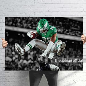 May include: A poster featuring an American football player in a green uniform, mid-jump, holding a football. The background is a black and white stadium scene. The player's uniform has the number 28. The poster is held by hands.