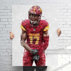 May include: A watercolor-style print of an American football player in a burgundy and gold uniform. The player is wearing a helmet and pads, with the number 17 visible. The word "COMMANDERS" is printed on the jersey. The player is celebrating with an open mouth and clenched fists.