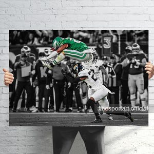 May include: A black and white action shot of a football game. A player in a green and white uniform leaps over another player in a white and black uniform. The background shows a crowd of people.