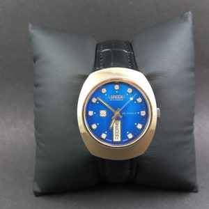 Könnte beinhalten: Eine goldfarbene Armbanduhr mit blauem Zifferblatt und diamantförmigen Stundenmarkierungen. Das Zifferblatt der Uhr trägt außerdem den Schriftzug "Lorenz Automatic 17 Jewels".