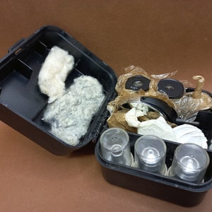 Könnte beinhalten: Ein schwarzer Plastikkoffer mit einer weißen Baumwollfütterung. Der Koffer enthält einen Satz Mikroskoplinsen, darunter zwei runde Linsen mit schwarzem Rand und eine größere runde Linse mit schwarzem Rand und silberner Mitte. Außerdem befinden sich vier klare Glasfläschchen mit schwarzen Kappen im Koffer.