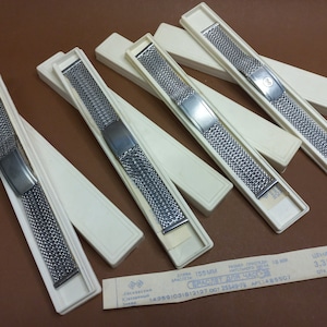 May include: Six silver watch bands in white boxes. The bands are made of a fine mesh metal and have a silver clasp. The boxes are labeled with the text "Браслет для часов" which translates to "Bracelet for watches".