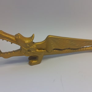 May include: A gold-colored dragon nutcracker with wings and a detailed design. The nutcracker is open, ready to crack nuts.