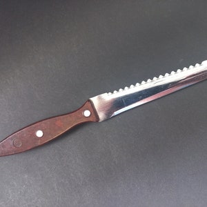 May include: A brown handled serrated knife with a silver blade. The knife is on a dark gray surface.