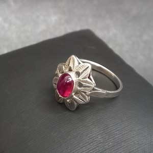 May include: A silver ring with a red gemstone set in a floral design.