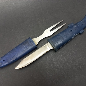 Puede incluir: Un juego de cuchillo y tenedor de plástico azul en forma de pez con una hoja y dientes plateados. El cuchillo y el tenedor están unidos por el mango.