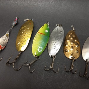 May include: Seven fishing lures with different colors and designs. The lures are made of metal and have a shiny finish. Some of the lures have a fish design, while others have a more abstract design.