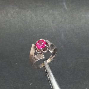 May include: A silver ring with a pink gemstone set in a flower-shaped design.
