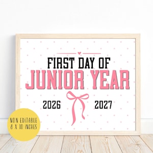 Könnte beinhalten: Ein rechteckiges Schild in einem hellen Holzrahmen mit weißem Hintergrund und rosa Punkten. Der Text lautet FIRST DAY OF JUNIOR YEAR in schwarzen und rosa Blockbuchstaben, ergänzt durch die Jahre 2026 und 2027 sowie eine rosa Schleife. Nicht editierbar 20,32 x 25,4 cm.