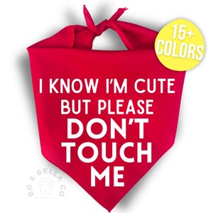May include: A bright red dog bandana with the text "I KNOW I'M CUTE BUT PLEASE DON'T TOUCH ME" in white. A yellow circle with "15+ COLORS" is in the upper right corner. The bandana is tied at the top.
