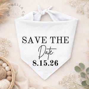 May include: White dog bandana with the text "SAVE THE Date" and the date "8.15.26" in black. The bandana is tied at the top. The Bo & Bella Co. logo is in the upper left corner.