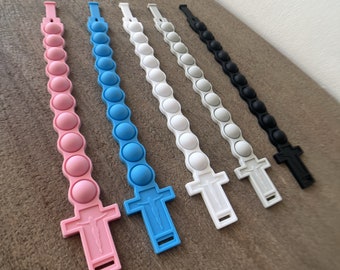 Può includere: Sei braccialetti in silicone con un ciondolo a forma di croce. I braccialetti sono rosa, blu, bianco, grigio, nero e grigio scuro. Ogni braccialetto ha una fila di 10 bottoni rotondi a forma di bolla.