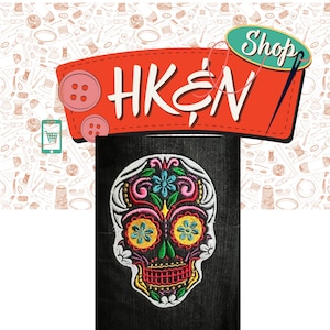 May include: A colorful embroidered skull patch with floral details. The skull is white with black outlines and features pink, yellow, blue, and green flowers. The patch is on a black fabric background.