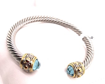 May include: A silver and gold twisted bangle bracelet with blue gemstone accents.