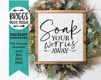 Puede incluir: Un letrero de madera con el texto "Soap Your Worries Away" en letra cursiva negra. El letrero está rodeado de una corona de hojas verdes y flores blancas.