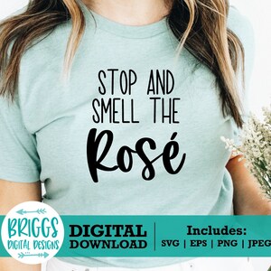 May include: A light blue t-shirt with the text "Stop and Smell the Ros&eacute;" in black. The shirt is being worn by a person holding a bouquet of white flowers.