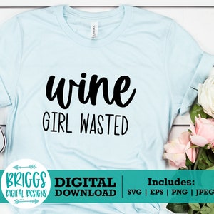 May include: A light blue t-shirt with the text "wine girl wasted" in black lettering. The shirt is laid flat on a white wooden surface with a bouquet of white and pink roses and a pair of white sneakers.