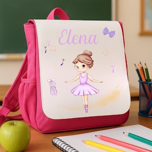 Puede incluir: Una mochila rosa con una solapa blanca con una ilustración de bailarina y el nombre "Elena" en escritura morada. El diseño incluye notas musicales y zapatillas de ballet. Una manzana y lápices están sobre el escritorio.