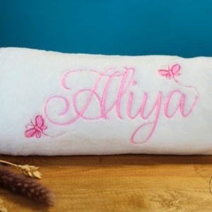 May include: White plush blanket with pink embroidery of the name "Aliya" and pink butterfly designs.
