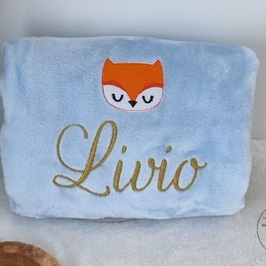 May include: A light blue plush blanket with a gold embroidered name "Livio" and a red fox face with black eyes.