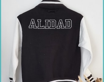 May include: Black and white varsity jacket with the word "ALIDAD" embroidered on the back. The jacket has white sleeves and a black body with white stripes around the collar, cuffs, and bottom.