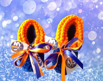 May include: A pair of handmade baby booties in blue, orange, and white. The booties feature a blue base, orange trim, and a ribbon with the NY Islanders logo. The booties are decorated with blue and orange ribbons.