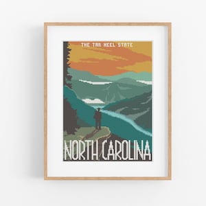 May include: A vintage-style poster featuring a pixelated image of a mountain landscape in North Carolina. The poster has a sunset sky with orange, yellow, and red hues. The text "The Tar Heel State" and "North Carolina" are printed in white on the poster.