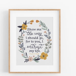 May include: A cross-stitch pattern featuring a floral wreath with yellow, pink, and blue flowers. The wreath surrounds the text "Show me the way I should go, for to you, I entrust my life. Psalm 119:8"
