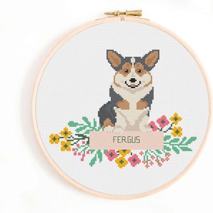 May include: Cross stitch pattern of a corgi dog with a floral wreath and a banner that says "FERGUS".
