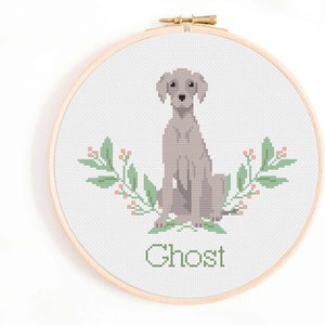 May include: Cross stitch pattern of a grey dog sitting with green leafy branches and pink berries on either side. The dog's name, "Ghost", is written below the dog.
