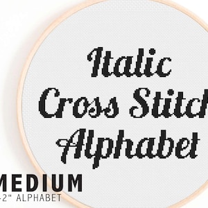 Może przedstawiać: Białe tamborek do haftu z czarnym tekstem, który brzmi "Italic Cross Stitch Alphabet" w ozdobnym kroju pisma. Tekst jest w średniej wielkości czcionki. Tamborek jest oznaczony "MEDIUM 1-2" ALPHABET"