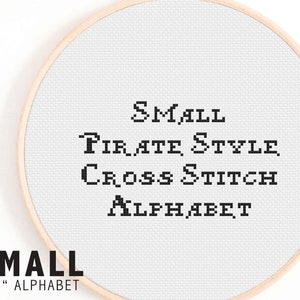 May include: A close-up of a white embroidery hoop with black text that reads "SMALL PIRATE STYLE CROSS STITCH ALPHABET". The text is in a pixelated font. The hoop is on a white background.