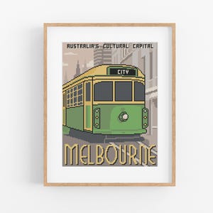 Op de afbeelding: Een ingelijste print met een pixelachtige illustratie van een groene en gele Melbourne-tram. De tekst "Australia's Cultural Capital" en "Melbourne" staan boven en onder de tram. Het woord "CITY" staat boven het voorste raam van de tram.