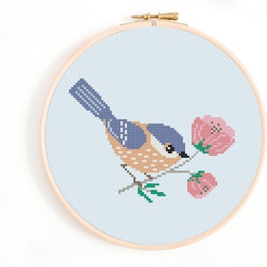 May include: A cross-stitch embroidery hoop with a blue bird perched on a branch with pink flowers. The bird is brown and blue with a light blue background.