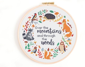 May include: Cross stitch pattern featuring a woodland scene with animals, mushrooms, and leaves. The text reads "Over the mountains and through the woods".